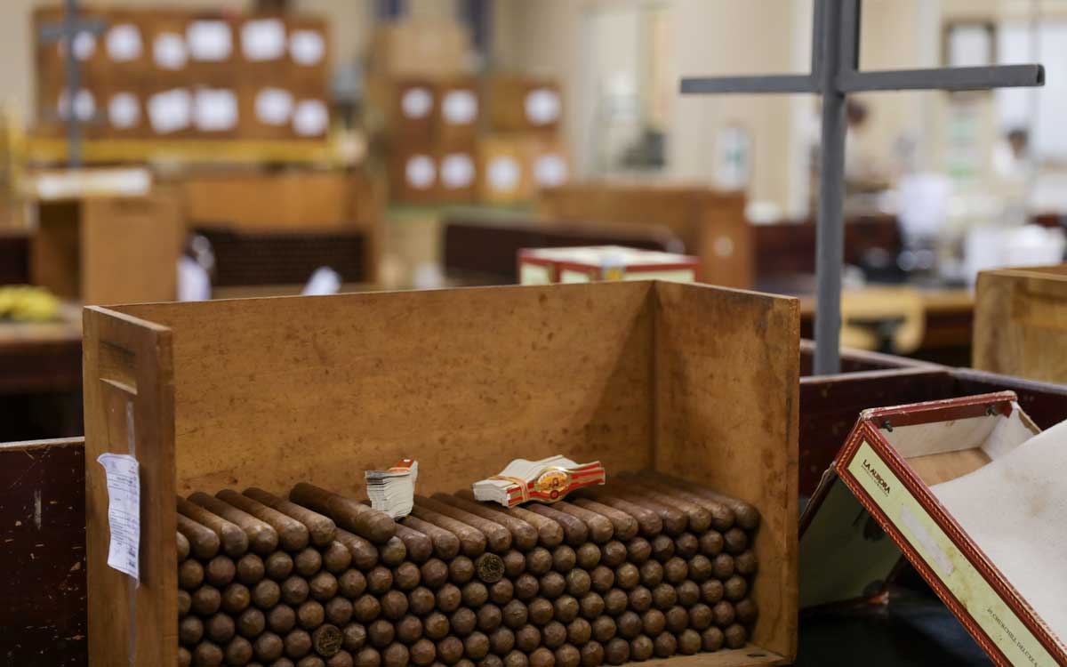 Handmade cigars piled in wooden box.